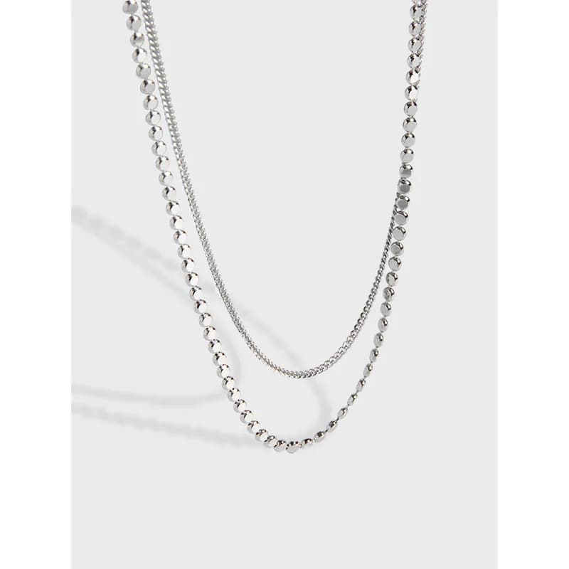 Two-layer sterling silver necklace with different chain styles hanging together against a light background.