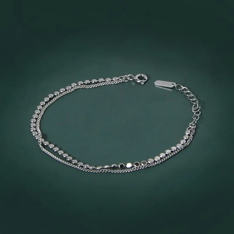 Polished sterling silver bracelet with two parallel disc chains and lobster clasp on a green backdrop.