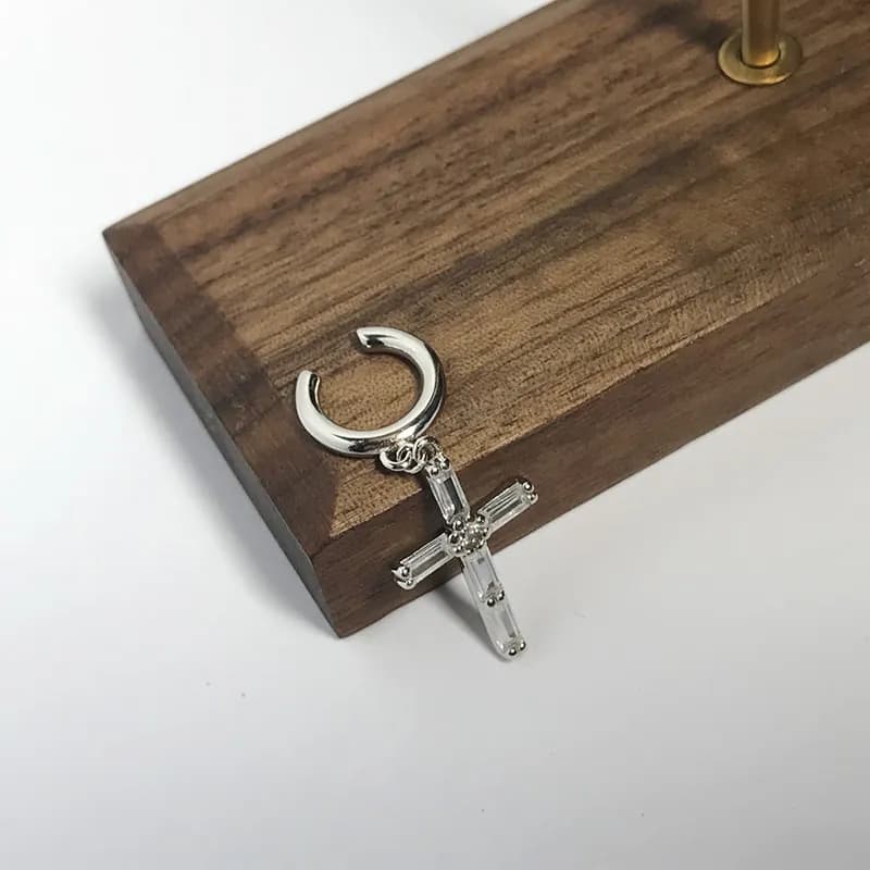Polished sterling silver hoop with a dangling baguette-crystal cross pendant on a wooden block