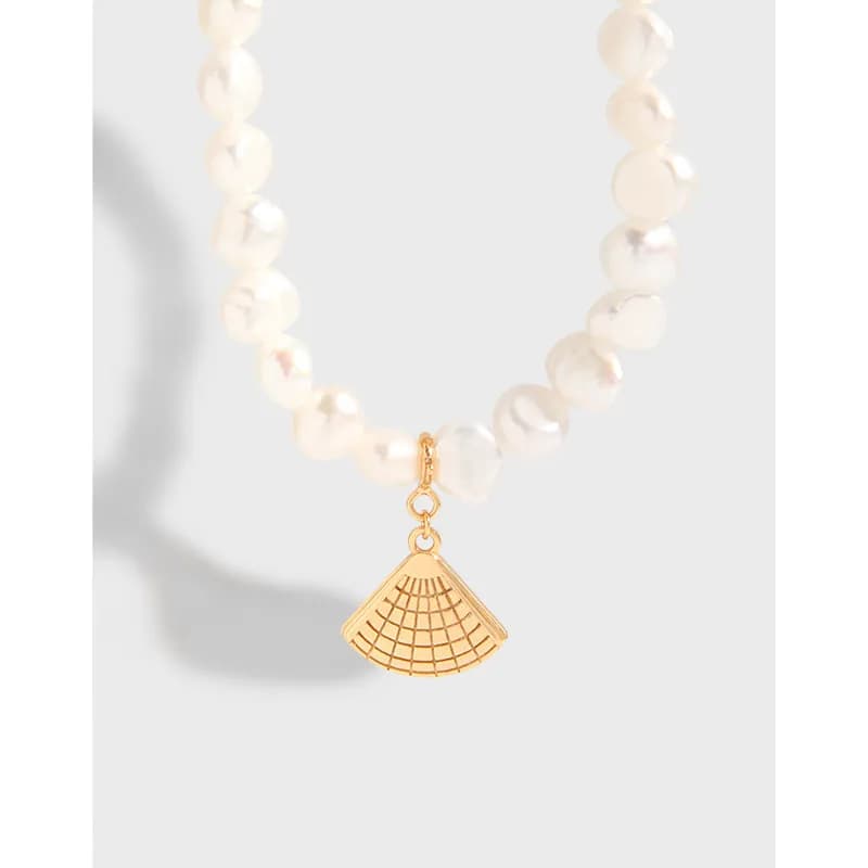 Close-up of a white beaded necklace with a gold-tone fan-shaped charm pendant centered on the chain.