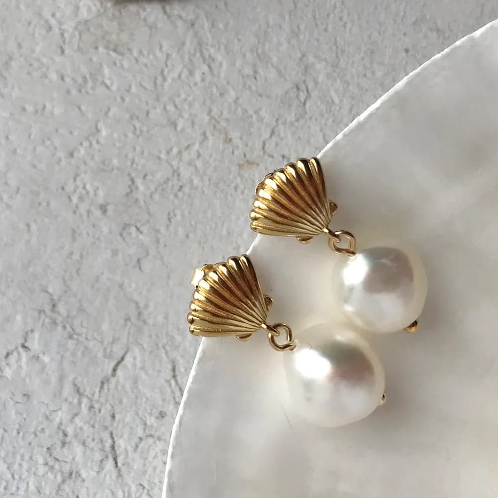 Gold-toned shell motifs sit above white pearls on a pair of drop earrings.