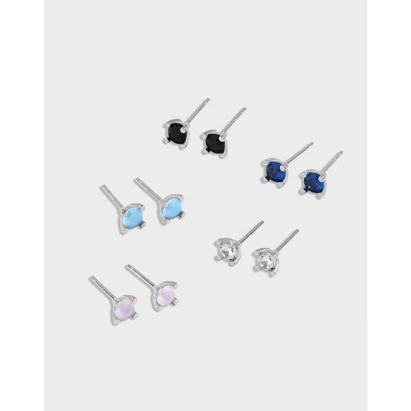 Small sterling silver stud earrings with round colored stones in prong settings arranged on a light background.