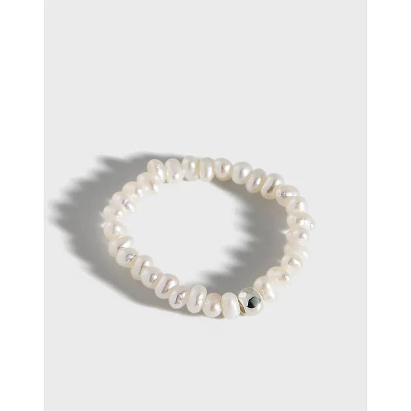A pearl bead ring sits on a light background, showcasing its small, rounded pearl beads forming a circular band.