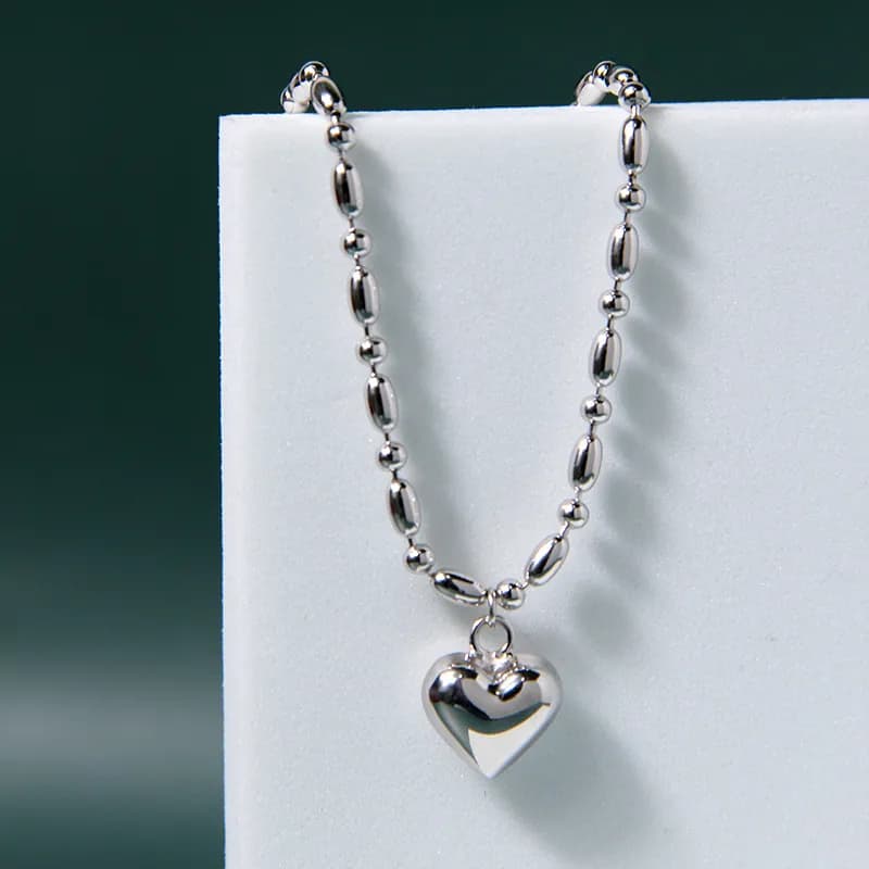 Polished sterling silver bracelet with a heart pendant displayed on a white surface.