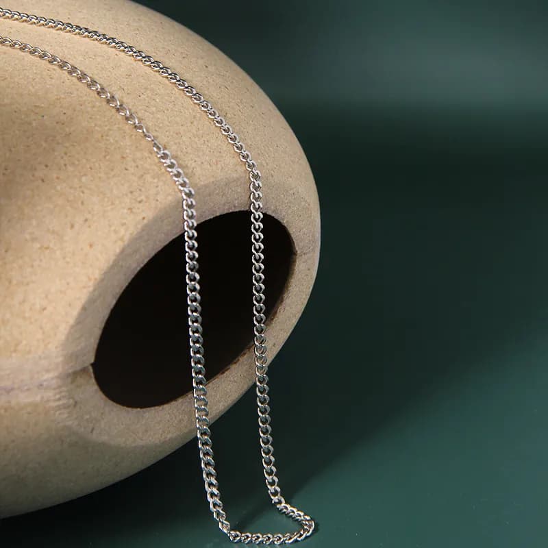 Polished sterling silver curb chain necklace draped over a beige ceramic form