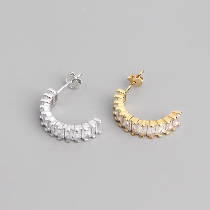 Two curved hoop earrings, one silver and one gold-tone, with rectangular stones along the outer arc.