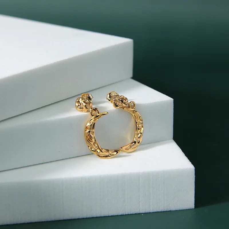 Polished sterling silver crescent hoop earrings with textured pattern resting on white steps.