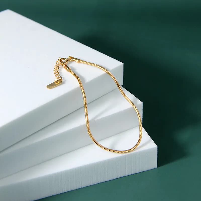 Polished sterling silver snake chain bracelet with extender and charm resting on white stacked blocks.