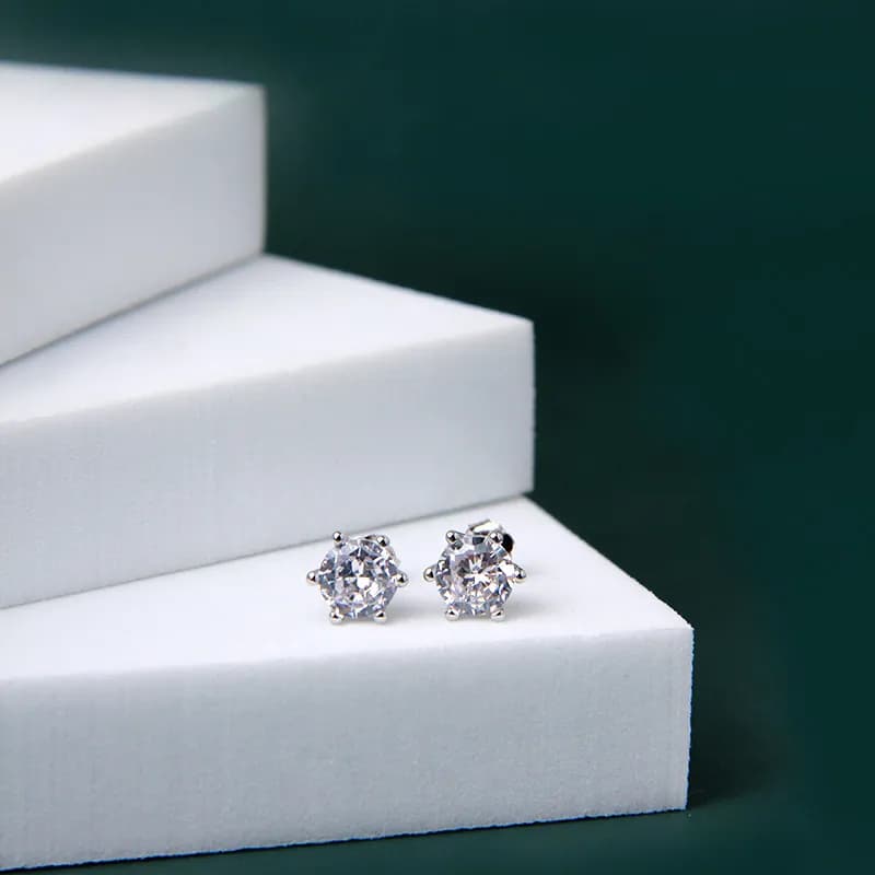 Round-cut clear studs in a polished silver setting displayed on white steps with a dark green background.