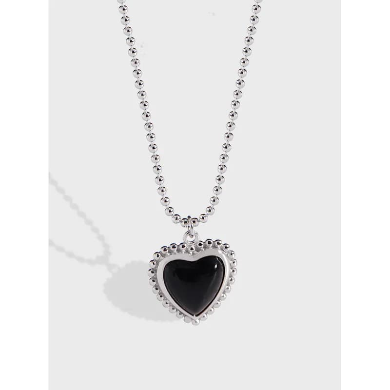 Close-up of a sterling silver bead chain necklace with a heart-shaped pendant featuring a black cabochon and dotted bezel