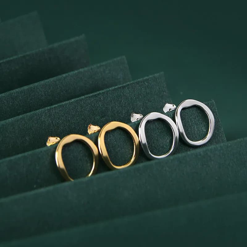 Polished oval hoop earrings in silver and gold tones arranged on a dark green surface.