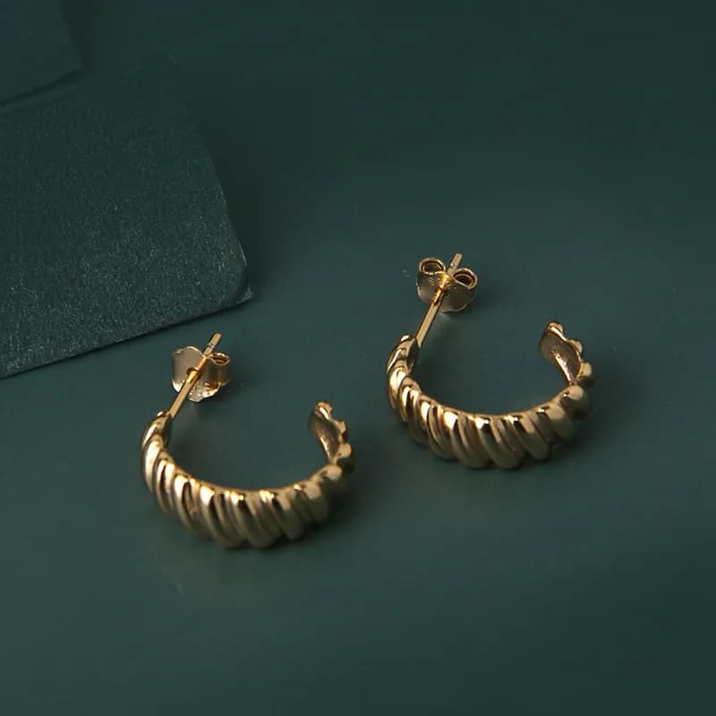 Polished sterling silver twisted rope hoop earrings with post backs displayed on a dark green surface.