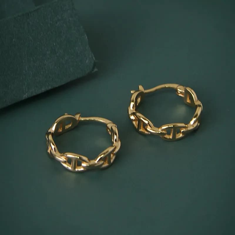 Polished sterling silver chain-link hoop earrings on a dark green surface.