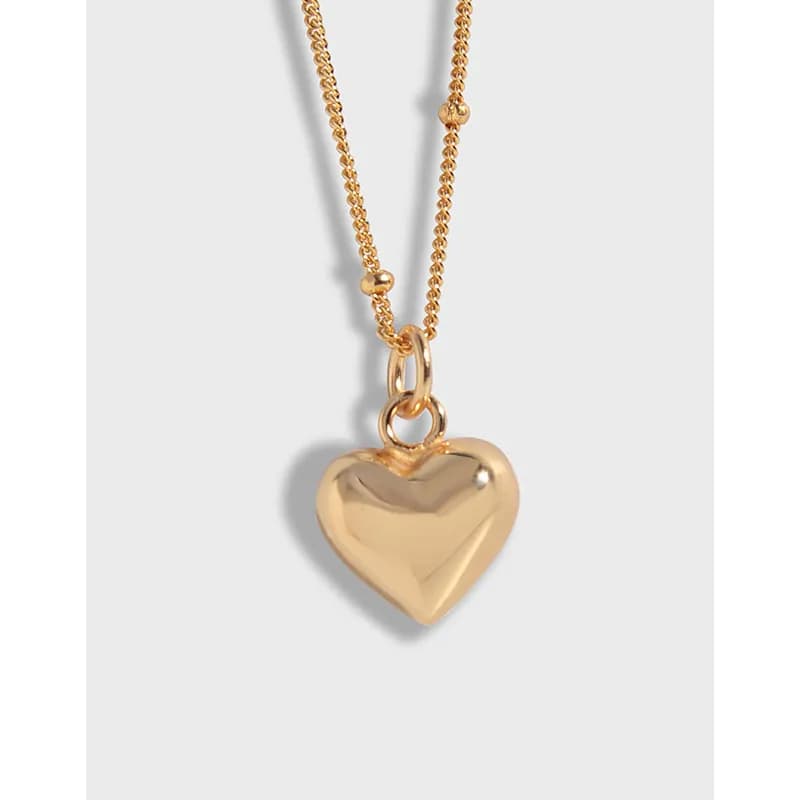 Close-up of a polished heart pendant on a fine chain against a neutral background.