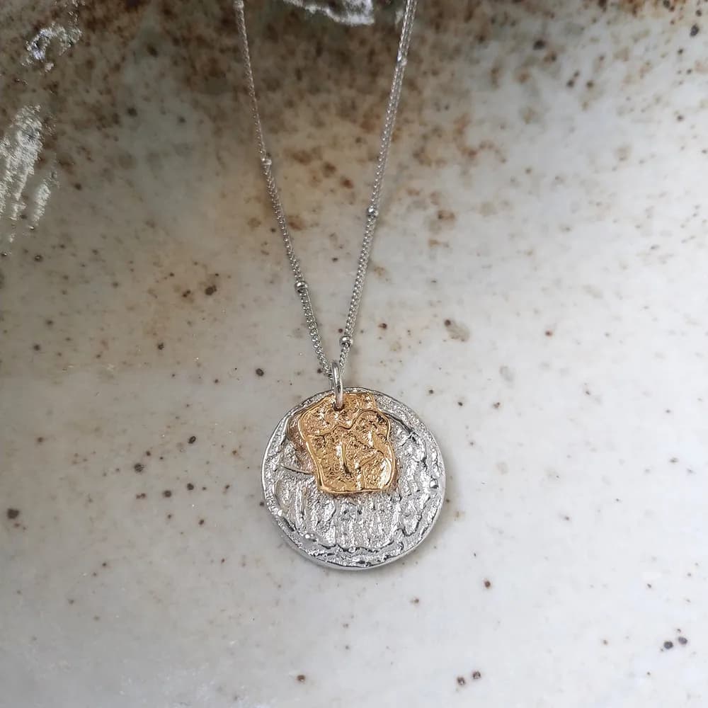 Polished sterling silver two-tone pendant necklace with a textured circular base and gold irregular overlay on a fine chain.