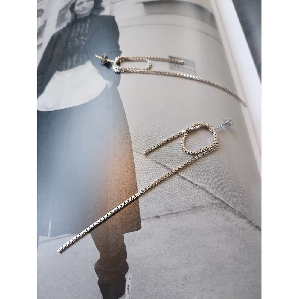 Polished sterling silver drop earrings with a long straight bar and small looping chain detail on a fashion magazine page.