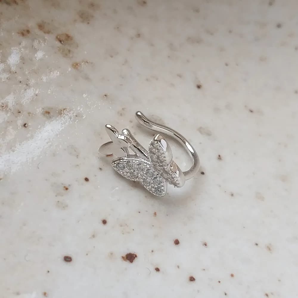 Open hoop silver earring with a pavé butterfly charm resting on a light marble surface.