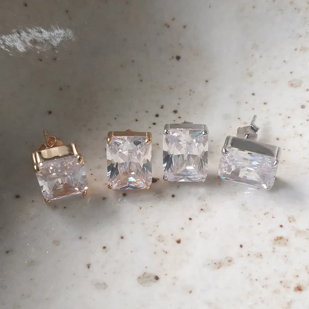 Close-up of four square-cut diamond-like stud earrings, two with gold-toned settings and two in silver, all with clear stones