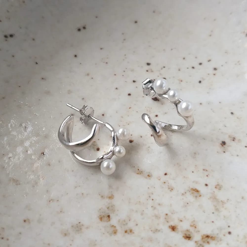Polished sterling silver curved hoop earrings with pearl accents along the outer edge.