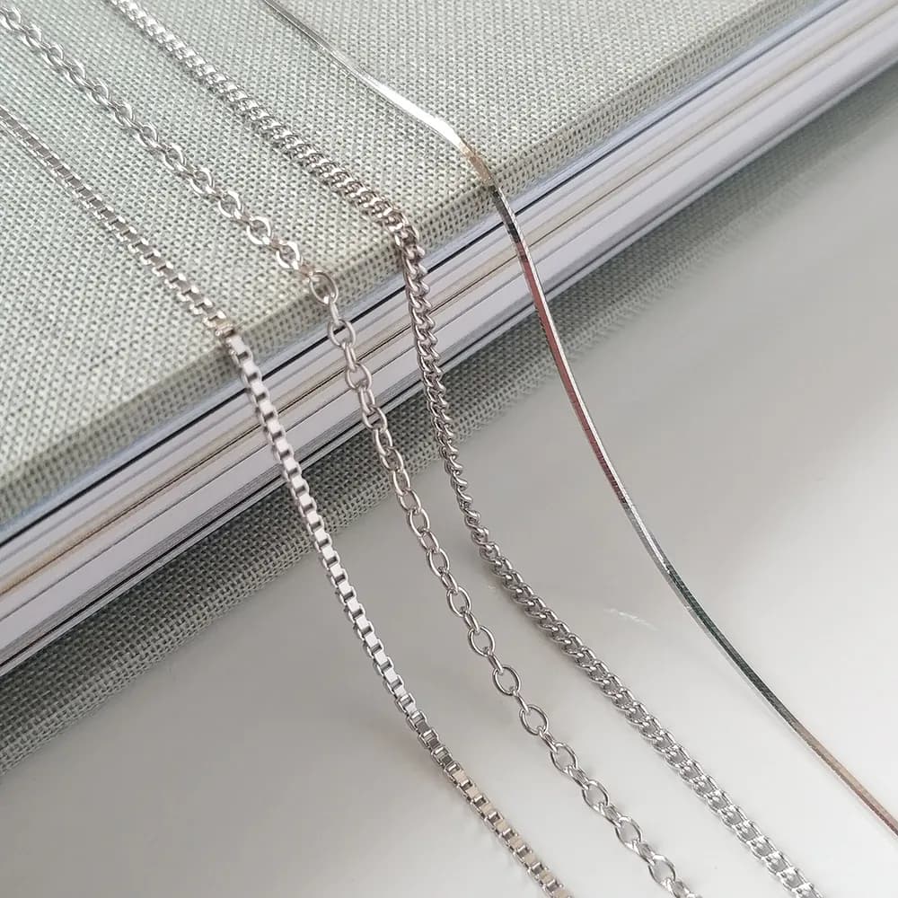 Close-up of multiple polished sterling silver chains with different link styles laid over a light book.