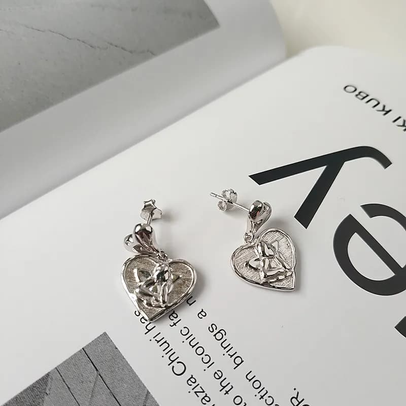 Polished sterling silver heart-shaped drop earrings with a floral motif on a white surface.