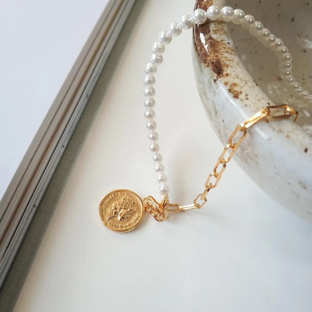 Two-tone pearl bead necklace with a gold coin charm resting near a marble surface.