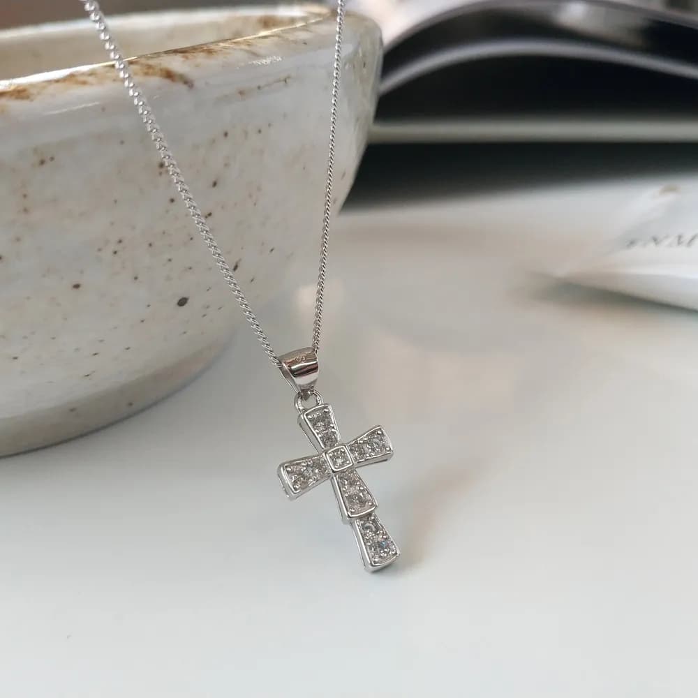 Polished sterling silver cross pendant on a slender chain, resting against a light surface.