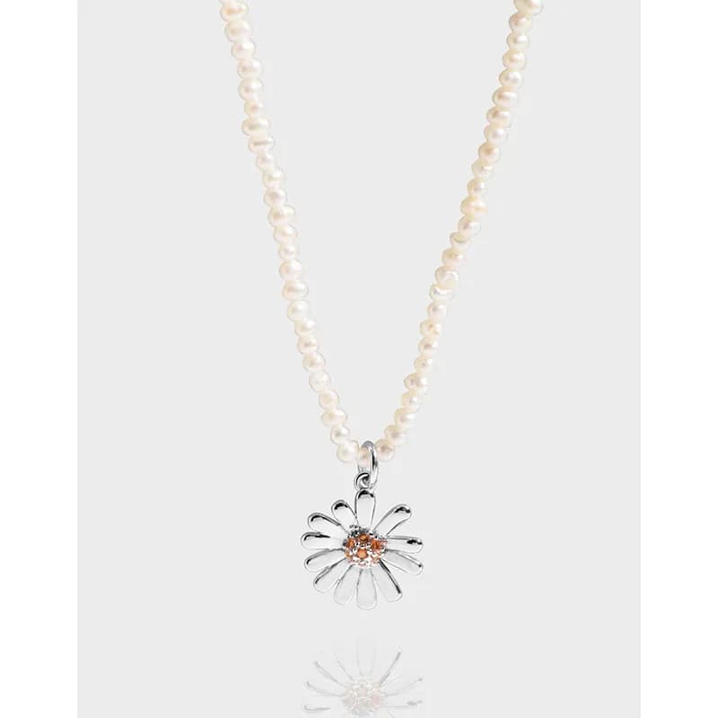 Pearl bead necklace with a silver daisy pendant hanging against a pale backdrop.