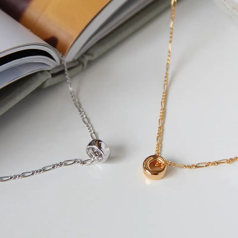 Two fine chain necklaces with small circular bead pendants in silver and gold, shown on a white surface.
