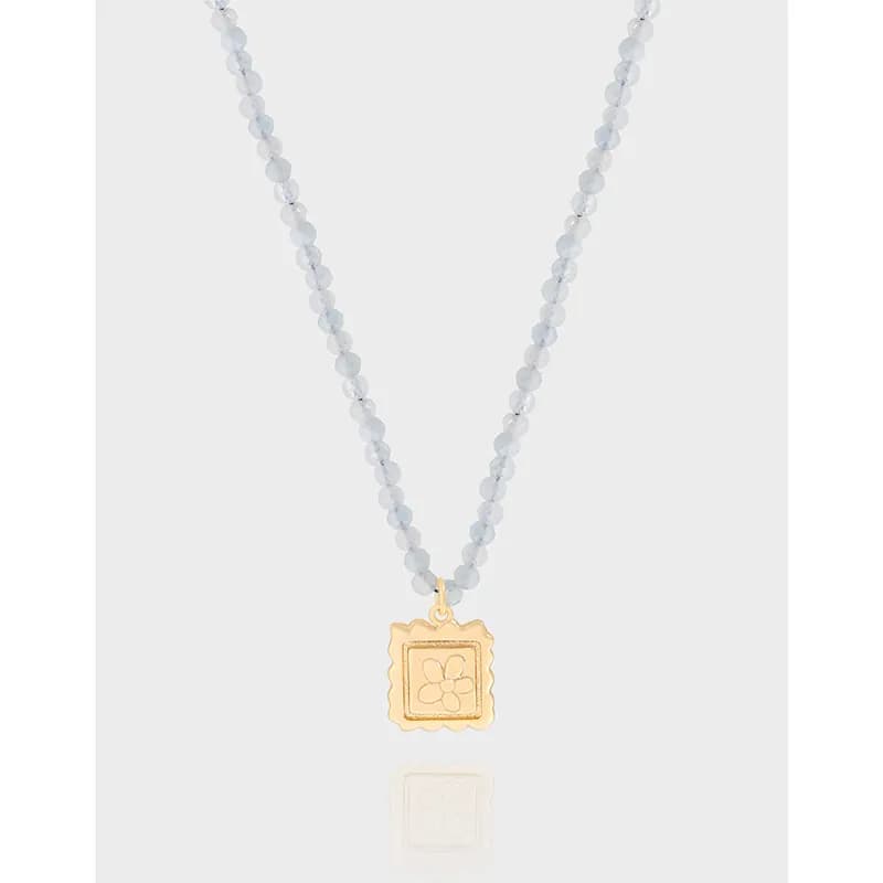 Close-up of a grey faceted bead necklace with a gold-tone square pendant featuring a floral design.