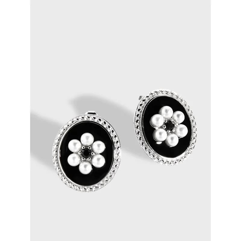 Sterling silver oval earrings with black enamel and pearl flower centerpiece set against a light background.