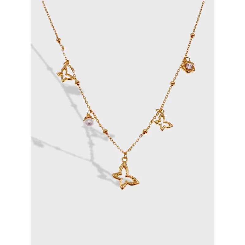 Polished gold-tone butterfly charm necklace with pearl and crystal accents on a delicate chain.