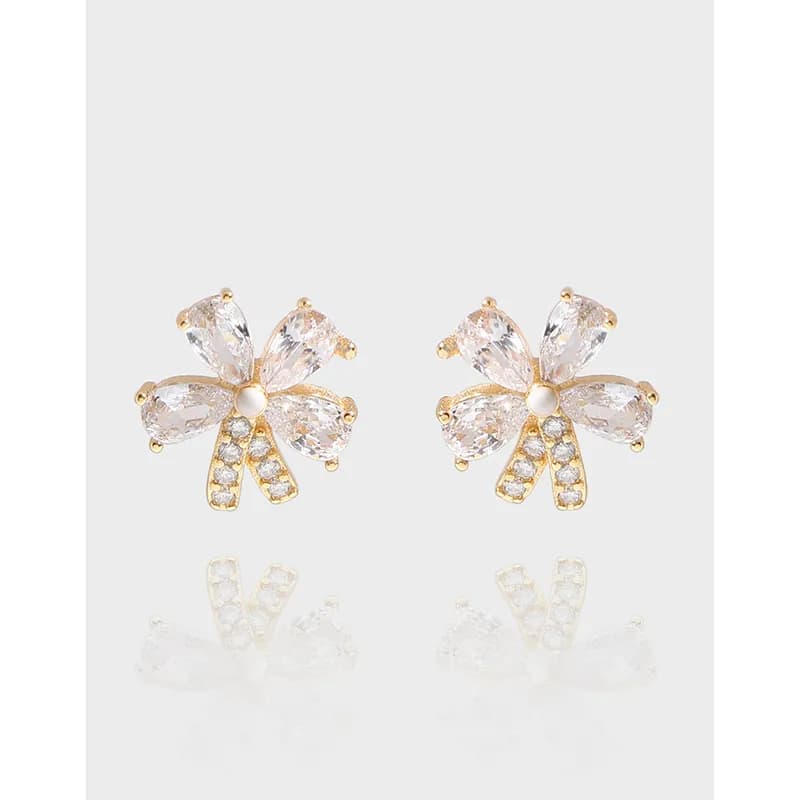 Flower-shaped crystal earrings with five teardrop petals around a central pearl on a polished surface.
