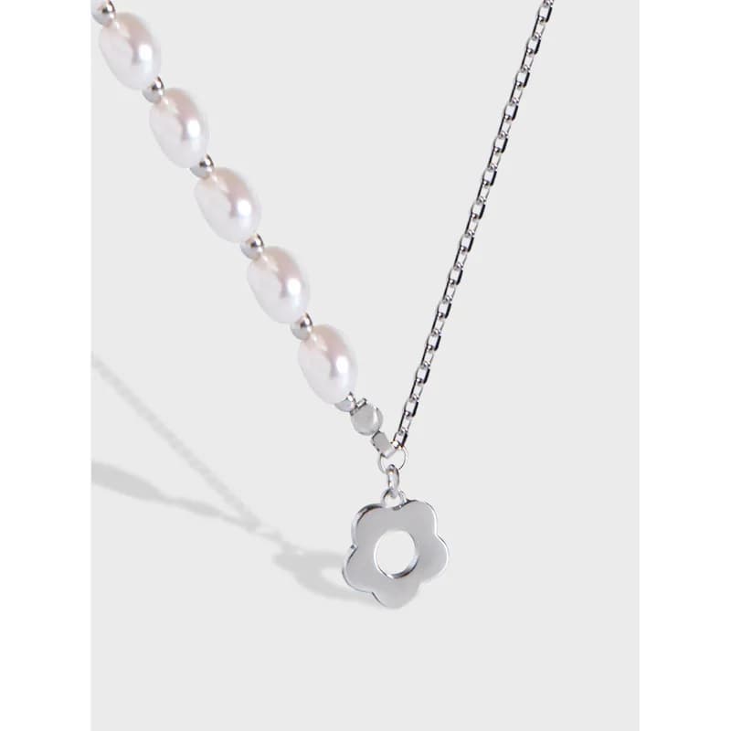 Close-up of a sterling silver necklace with pearl beads on one strand and a flower-shaped pendant on a polished chain.