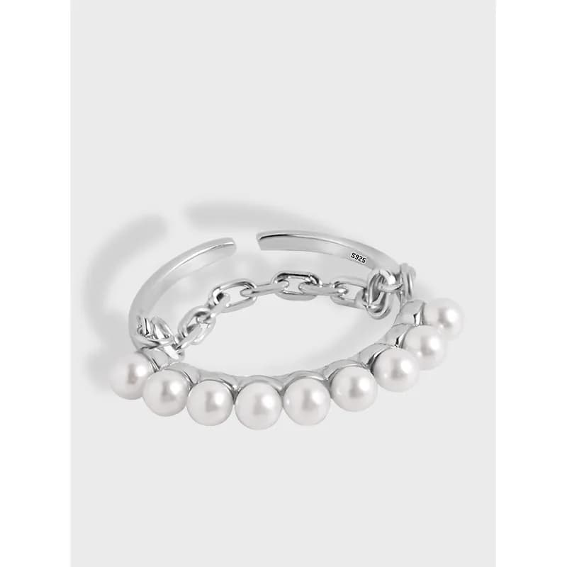 Close-up of a polished sterling silver ring with a row of white pearls and chain-link accents.