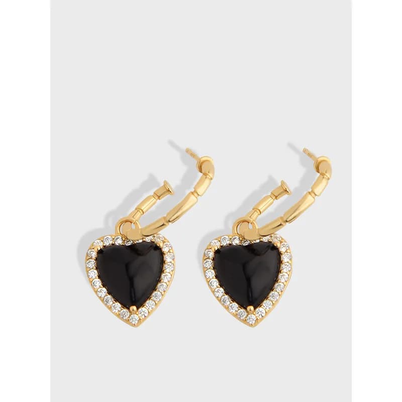 Close-up of gold-tone hoop earrings each with a black enamel heart surrounded by a clear crystal halo.