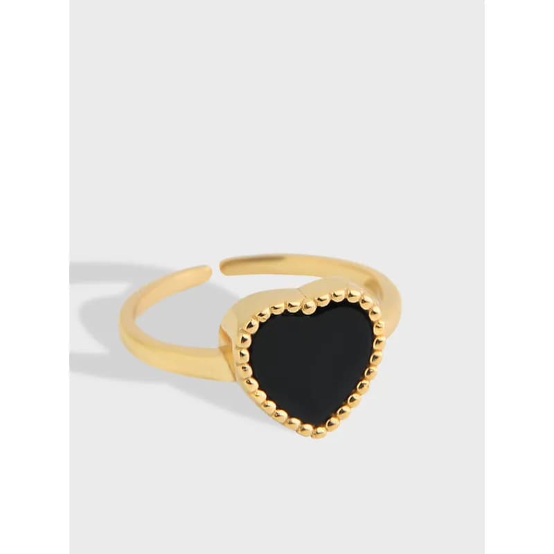 Close-up of a heart-shaped ring with a black center and beaded bezel on an open, gold-tone band.