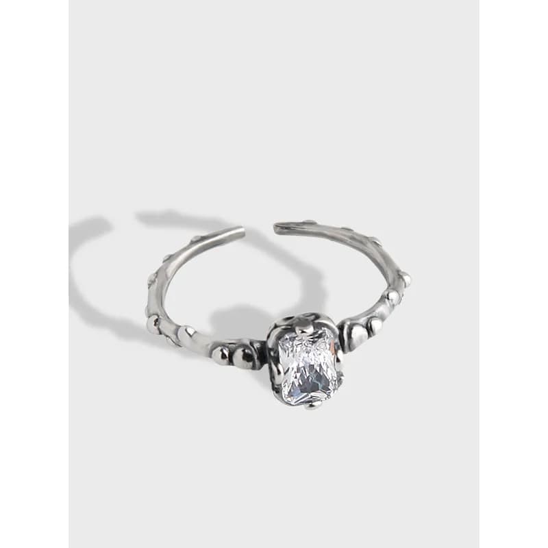 Matte sterling silver ring with a cushion-cut clear gemstone and a textured beaded band.