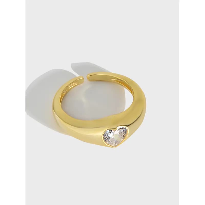 Gold-tone polished ring with a heart-shaped clear crystal front detail on an open-band design.