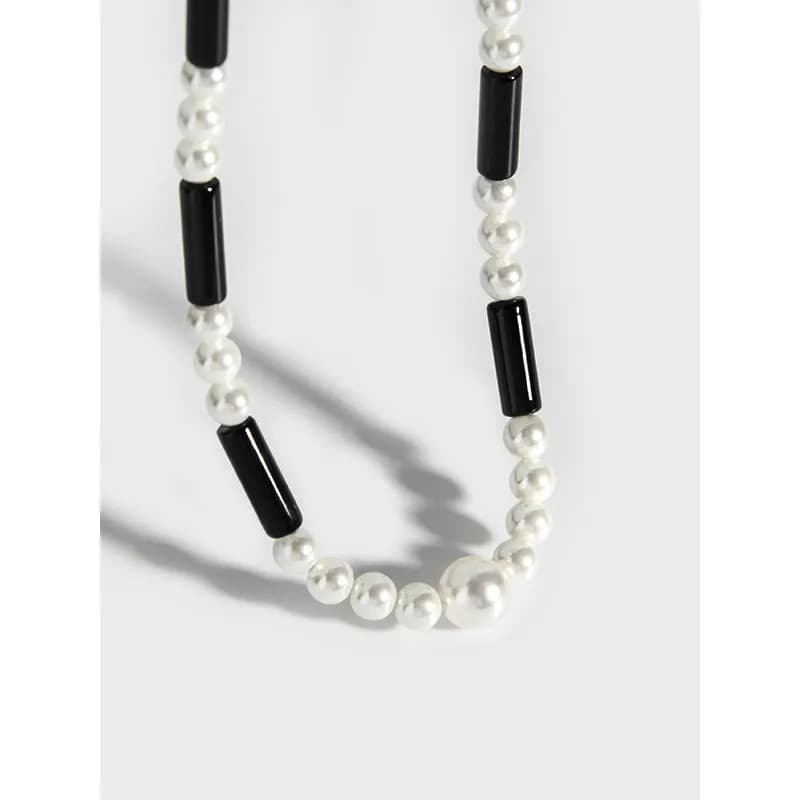 Close-up of a pearl and black bar necklace showing alternating pearls and black cylindrical beads on a polished silver chain.
