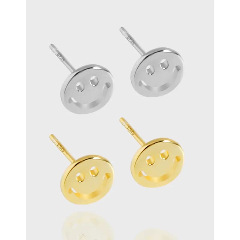Polished round smiley-face disk stud earrings in silver and gold-tone finishes on a light background.
