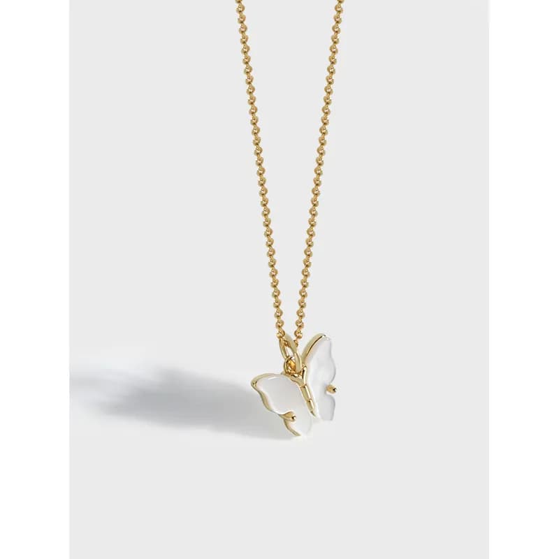 Delicate necklace with two white enamel butterfly charms on a slim chain against a light background.