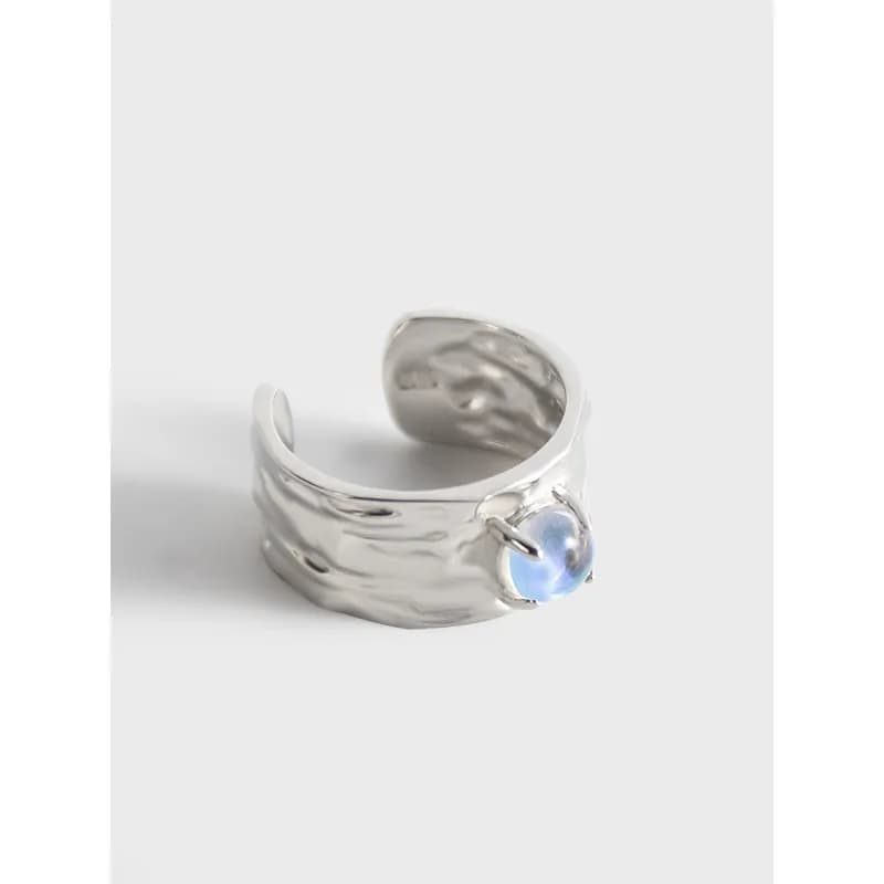 A wide polished sterling silver ring with a hammered texture and a blue iridescent moonstone cabochon set on the side.