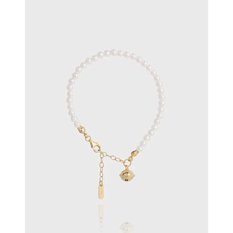 Pearl bead bracelet with gold-tone chain and dangling charms on a light background.