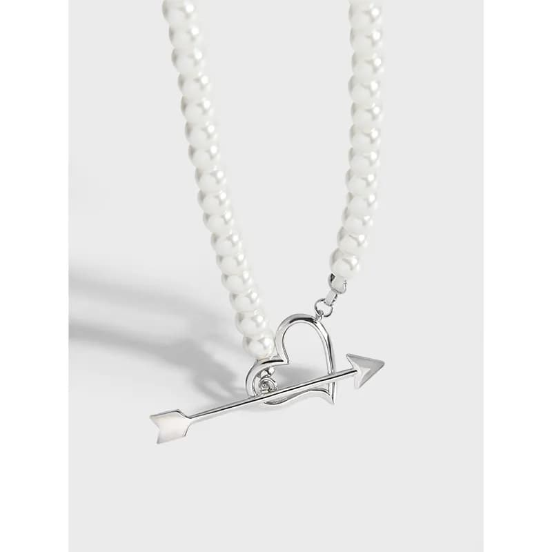 A pearl bead necklace draped with a silver heart and arrow pendant hanging at center.