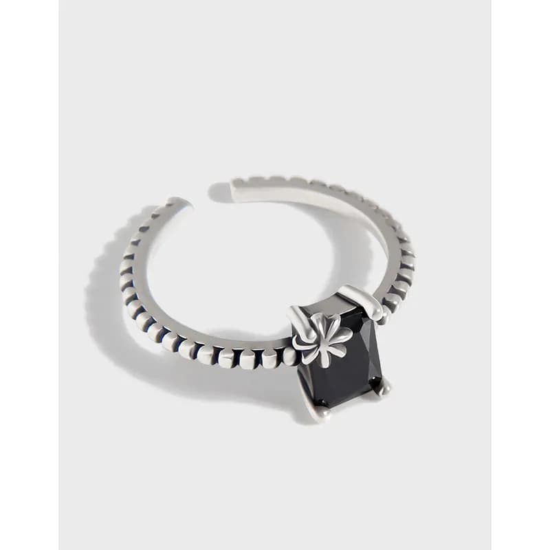 Open sterling silver ring with a square black gemstone and a small floral accent on a beaded band.