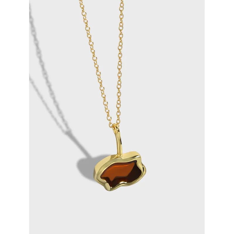 Close-up of a gold-tone pendant with an irregular brown stone on a delicate chain.