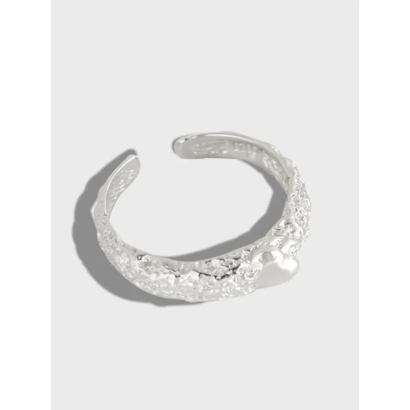 Open cuff ring in polished sterling silver with a textured surface and a small heart detail.