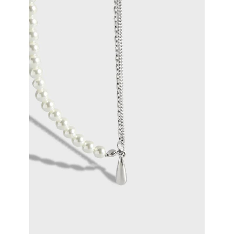 Close-up of a two-tone necklace with a pearl strand and a silver chain meeting at a teardrop pendant.