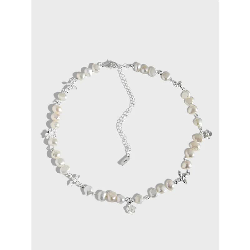 Close-up of a polished silver necklace with irregular white pearls and tiny flower charms on a light background.